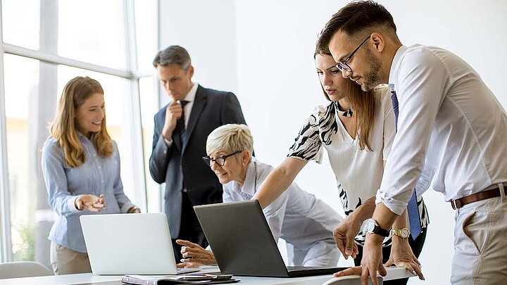 Gruppe Personen mit Laptop arbeiten gemeinsam an einem Tisch.